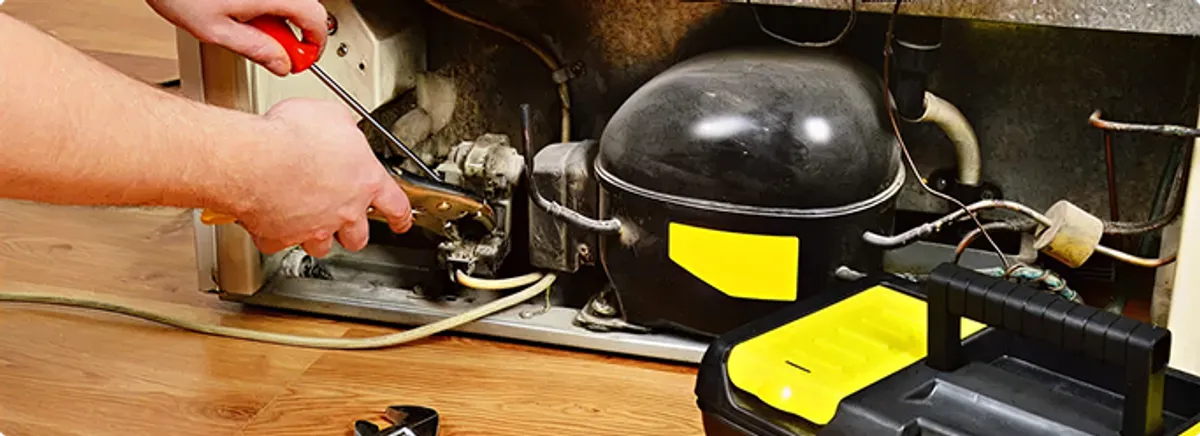 Refrigerator repair technician fixing the compressor and wiring in Louisville, KY